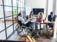 Lavoro e disabilità: young businessman in wheelchair working with colleagues in office
