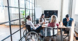 Lavoro e disabilità: young businessman in wheelchair working with colleagues in office